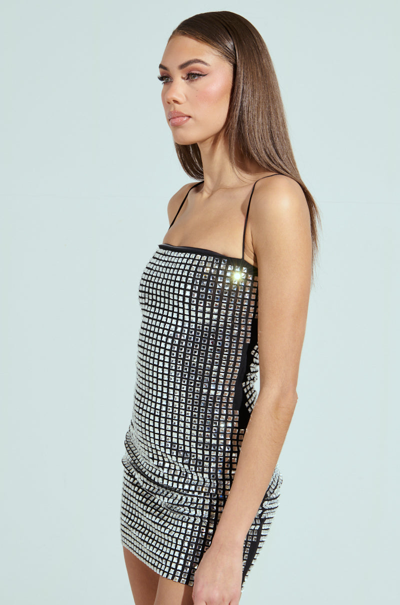 A woman with long brown hair wears the sleeveless IN MY ELEMENT RHINESTONE MESH MINI DRESS. She stands sideways against a light grey background, the bodycon silhouette accentuating her figure as she looks forward with a calm expression.