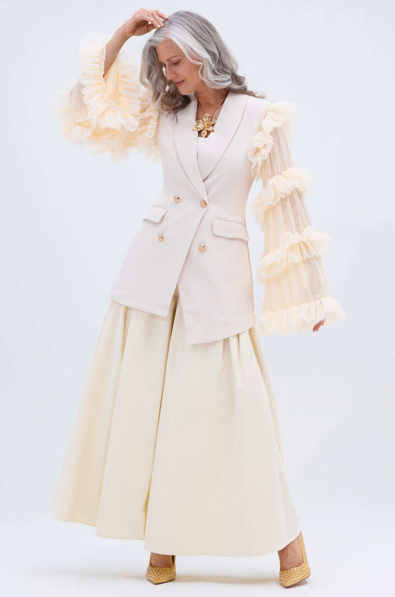 A woman with long gray hair poses gracefully in a cream blazer, statement necklace, and TAY TAY TROUSER—a wide-leg, non-stretch cotton style—against a plain white background.