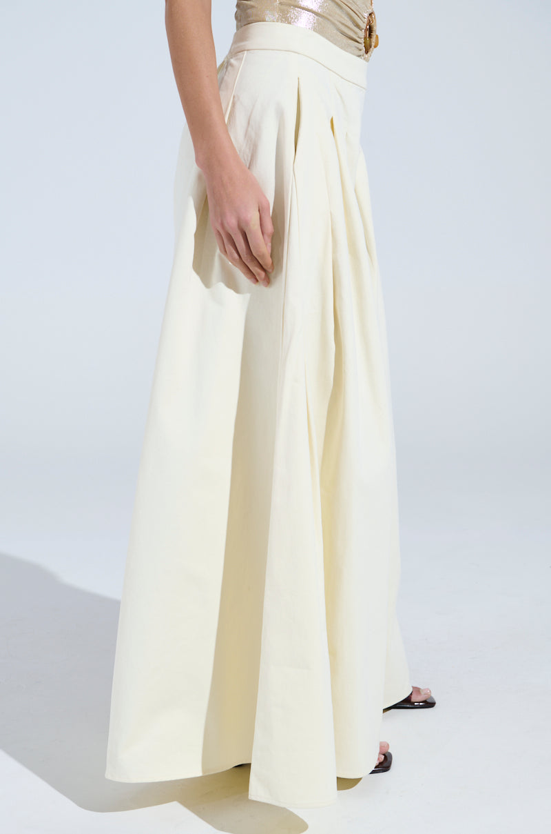 Someone is wearing a metallic sleeveless top and beige TAY TAY TROUSER with ultra-wide legs and pleats, highlighted from the side against a neutral backdrop.