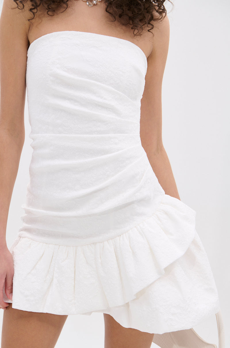 The GARDEN PARTY MINI DRESS IN WHITE features a strapless, fitted bodice, textured fabric, and ruffled asymmetrical hem—perfect for any garden party. Shown against a plain white background.