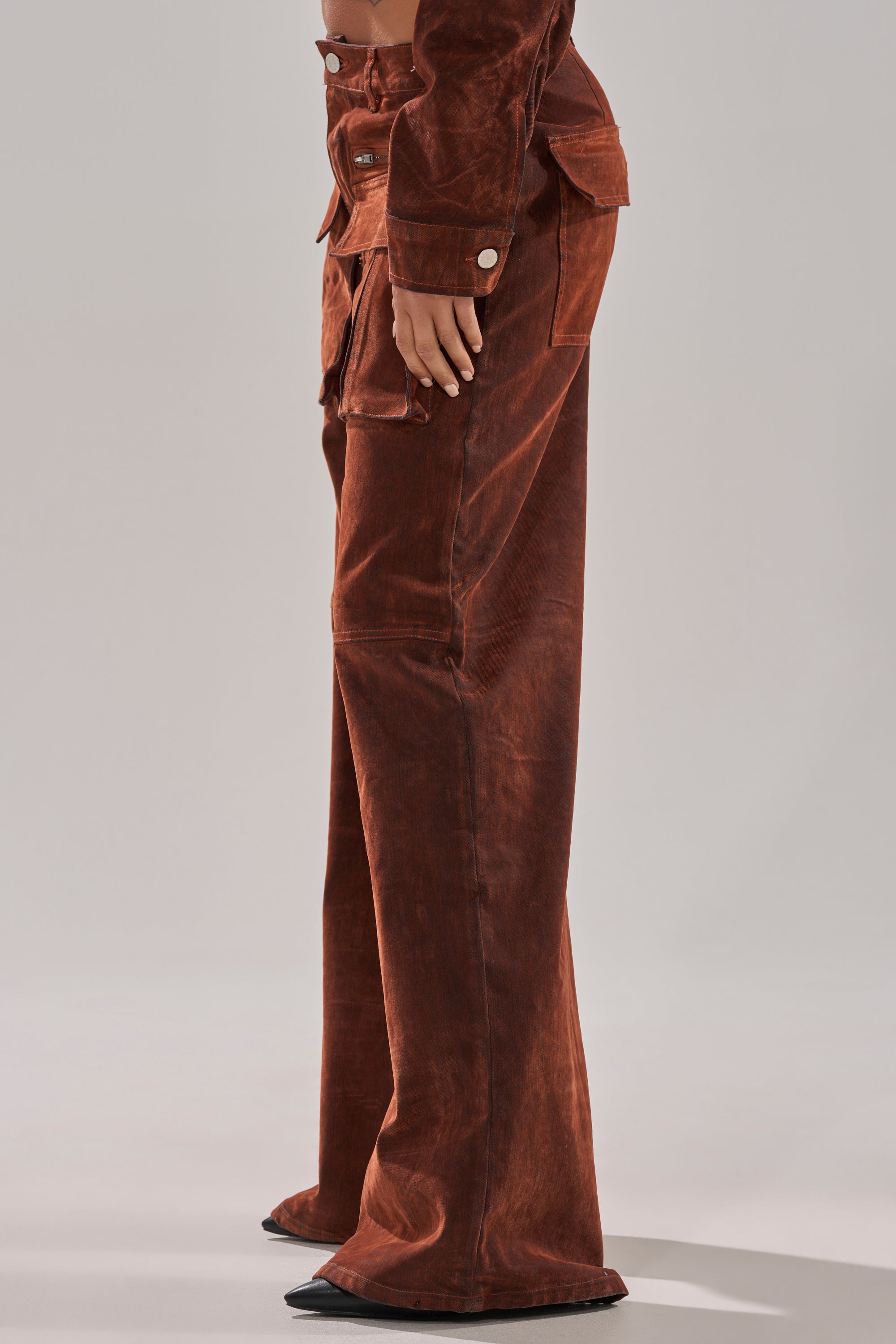 A person wears the THINK ABOUT YOU ALL THE TIME VELVET DENIM CARGO TROUSER in orange with wide legs, visible seams, and pockets, paired with a matching jacket. Only their lower body is visible against a plain background.