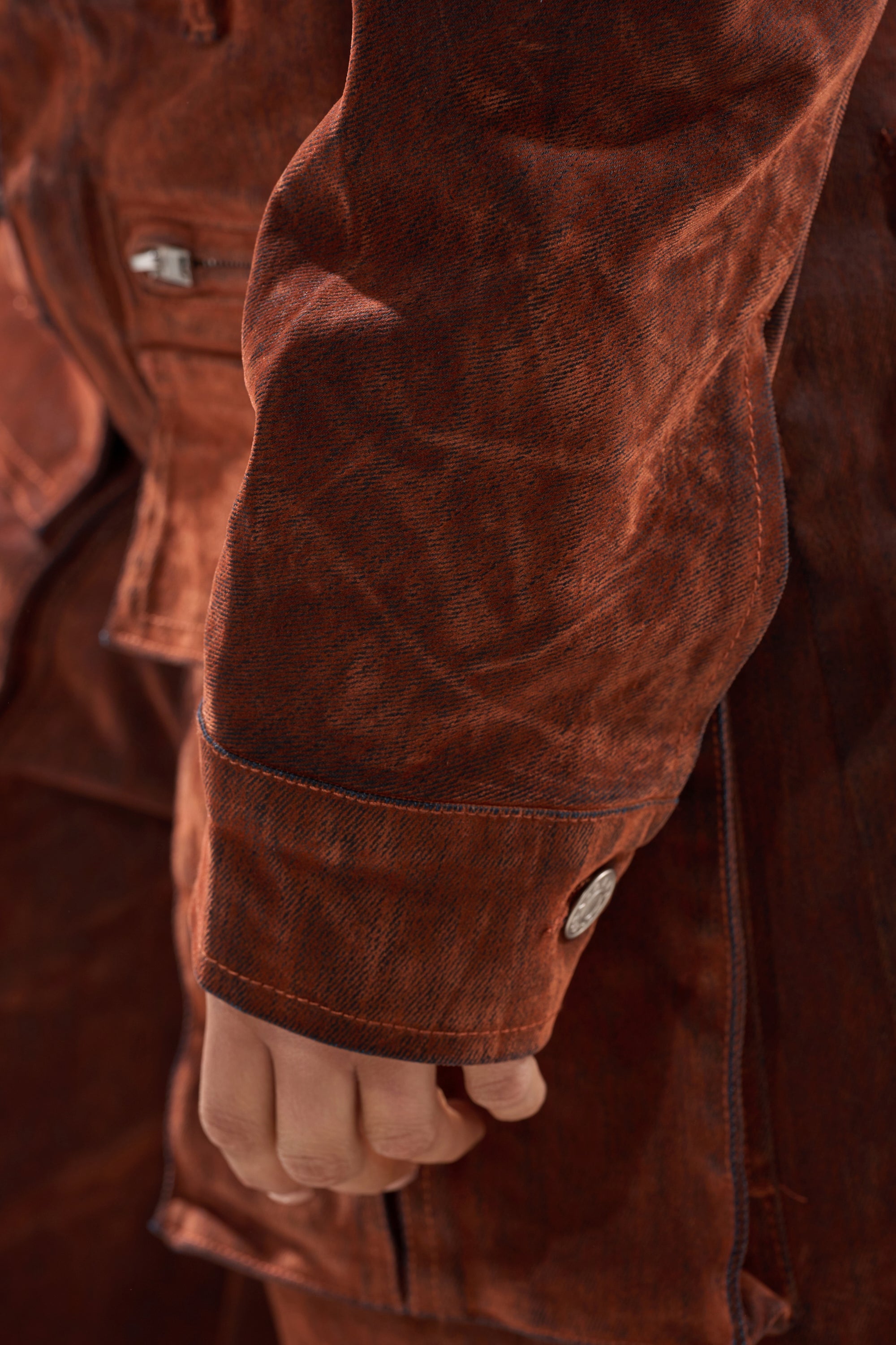 Close-up of a person’s hand at their side, wearing the THINK ABOUT YOU ALL THE TIME VELVET DENIM LONG SLEEVE TOP in rust with a visible cuff and silver button, paired with matching velvet denim pants.