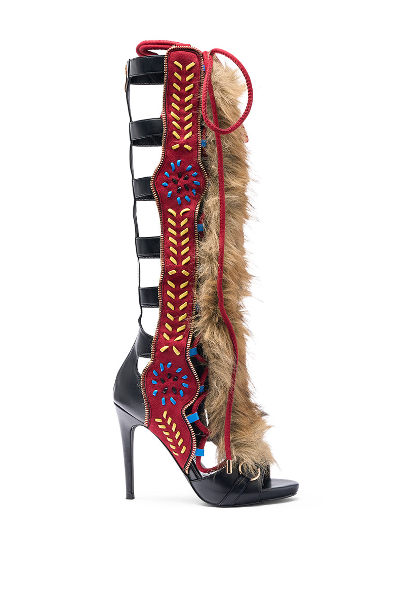 The AZALEA WANG SHAINE BLACK MULTI GLADIATOR STITCH AND FUR SANDAL features a high stiletto heel, open toe, black straps with red embroidery, blue and yellow accents, and brown faux fur trim along the side.