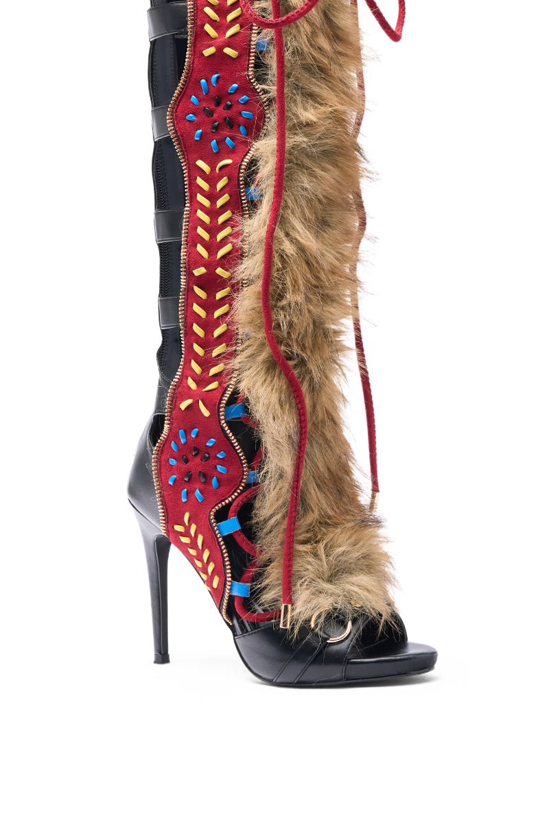 The AZALEA WANG SHAINE BLACK MULTI GLADIATOR STITCH AND FUR SANDAL is a bold knee-high open-toe stiletto boot that features black leather, red suede, blue and yellow embroidery, brown faux fur, and red lace-up details.