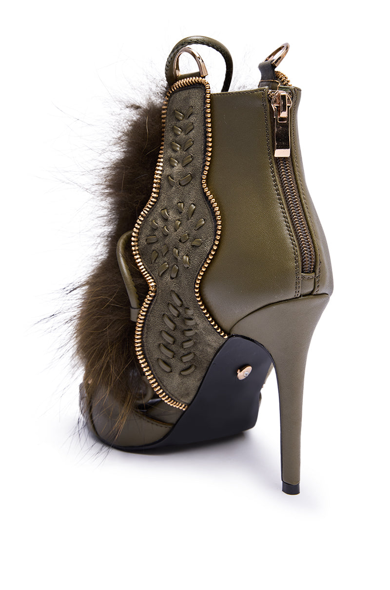 The AZALEA WANG SHAINY OLIVE FUR SANDAL features an olive green finish, decorative side panel, fur trim, gold heel zipper, intricate stitching, and a tall stiletto heel for a fashionable and striking look.