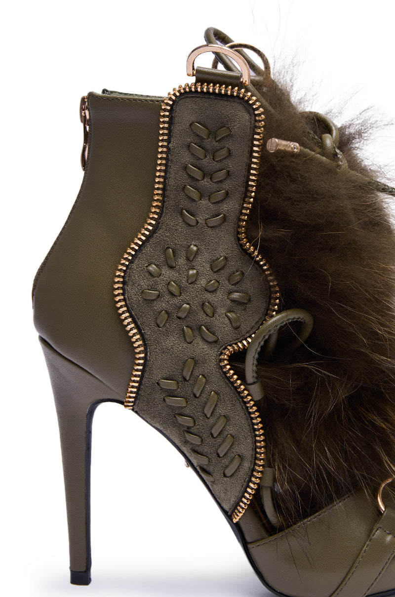 The AZALEA WANG SHAINY OLIVE FUR SANDAL features an olive green stiletto heel with decorative stitching, metal accents, a fuzzy brown fur trim, zipper detail along the edge, and lace-up accents for extra flair.