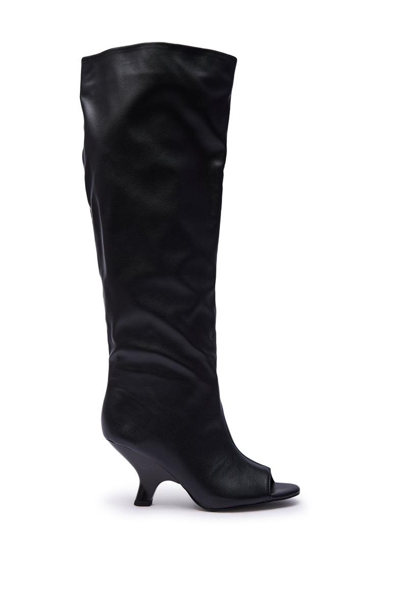 The AZALEA WANG SIZANI Black Wedge Slouchy Boot is a knee-high, black faux leather boot featuring a peep toe, short curved wedge heel, and slightly shiny finish.