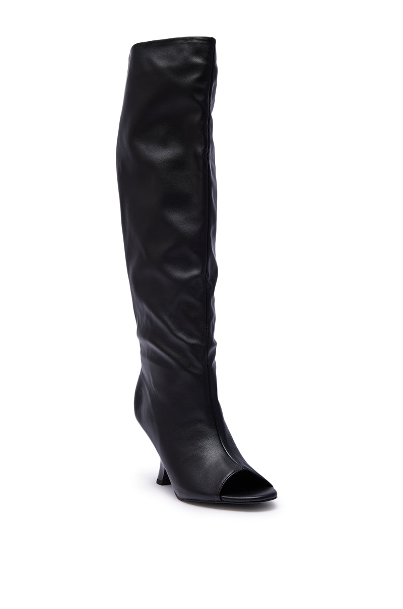 The AZALEA WANG SIZANI Black Wedge Slouchy Boot is a single knee-high faux leather boot with a mid-height wedge heel and an almond peep toe, shown against a white background.