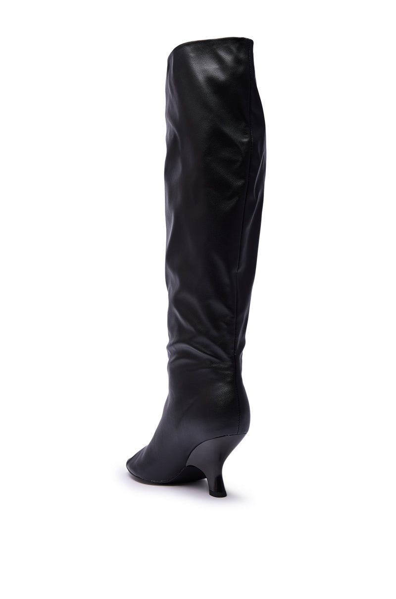 The AZALEA WANG SIZANI BLACK WEDGE SLOUCHY BOOT is a knee-high black faux leather boot with a pointed toe and wedge heel, displayed from the side against a white background.