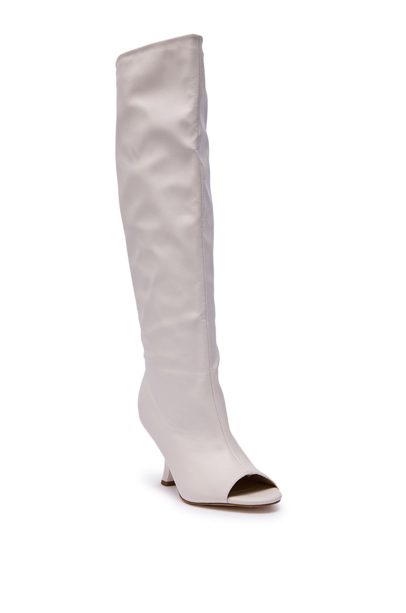 The AZALEA WANG SIZANI WHITE WEDGE SLOUCHY BOOT is a tall, white faux leather knee-high boot featuring a wedge heel and open toe, shown against a plain white background.