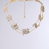 The STAY BLESSED NECKLACE is a faux gold piece featuring ornate, interlinked rhinestone letters encrusted with small diamonds. It has a dual-layer adjustable chain with a dangling clasp, set against a neutral background.