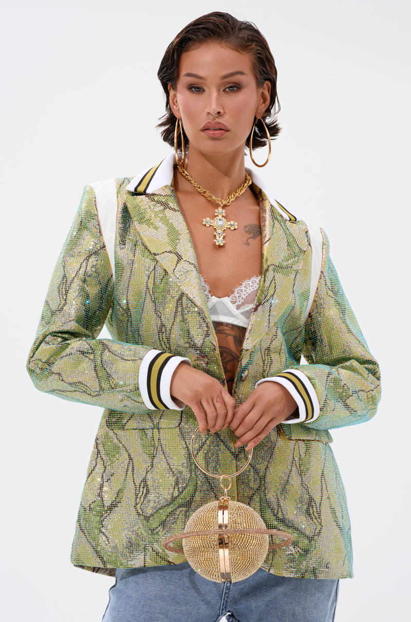A stylish woman poses confidently in the DON'T TRY ME EMBELLISHED BROCADE BLAZER, paired with a white lace bralette, light blue jeans, gold hoop earrings, a cross necklace, and a gold spherical purse with a ring handle.