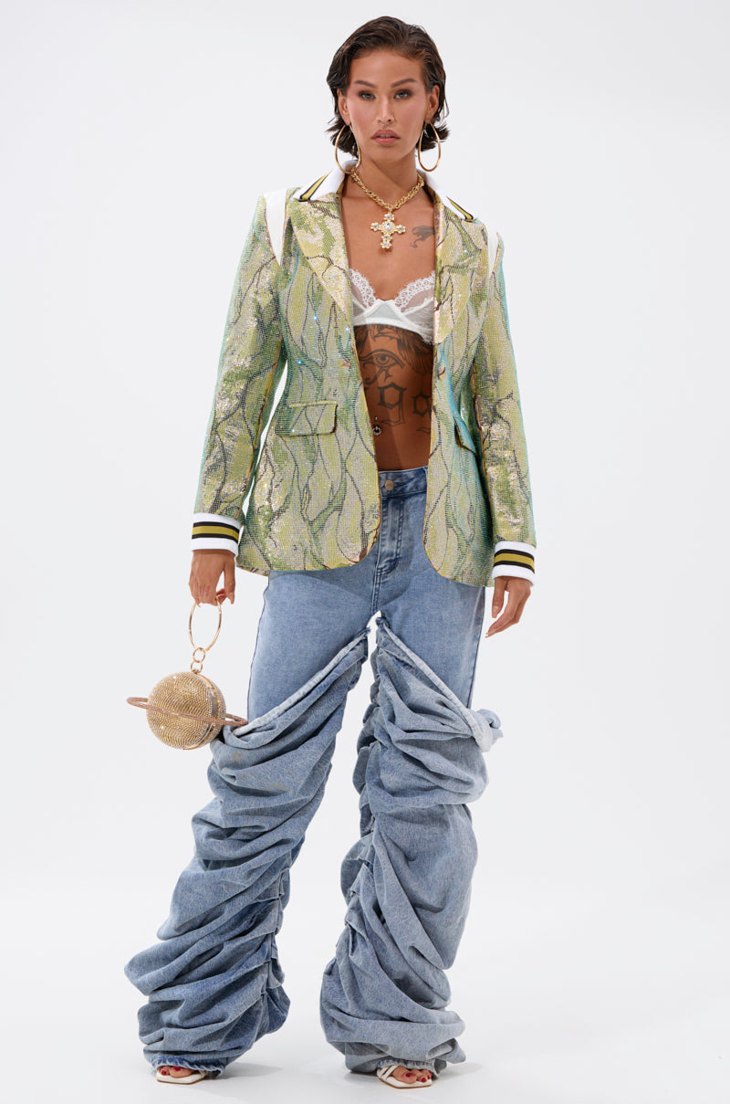 A model stands confidently in the DON'T TRY ME EMBELLISHED BROCADE BLAZER over a white lace bralette, baggy ruched jeans, chunky jewelry, and holding a small round handbag against a plain white background.