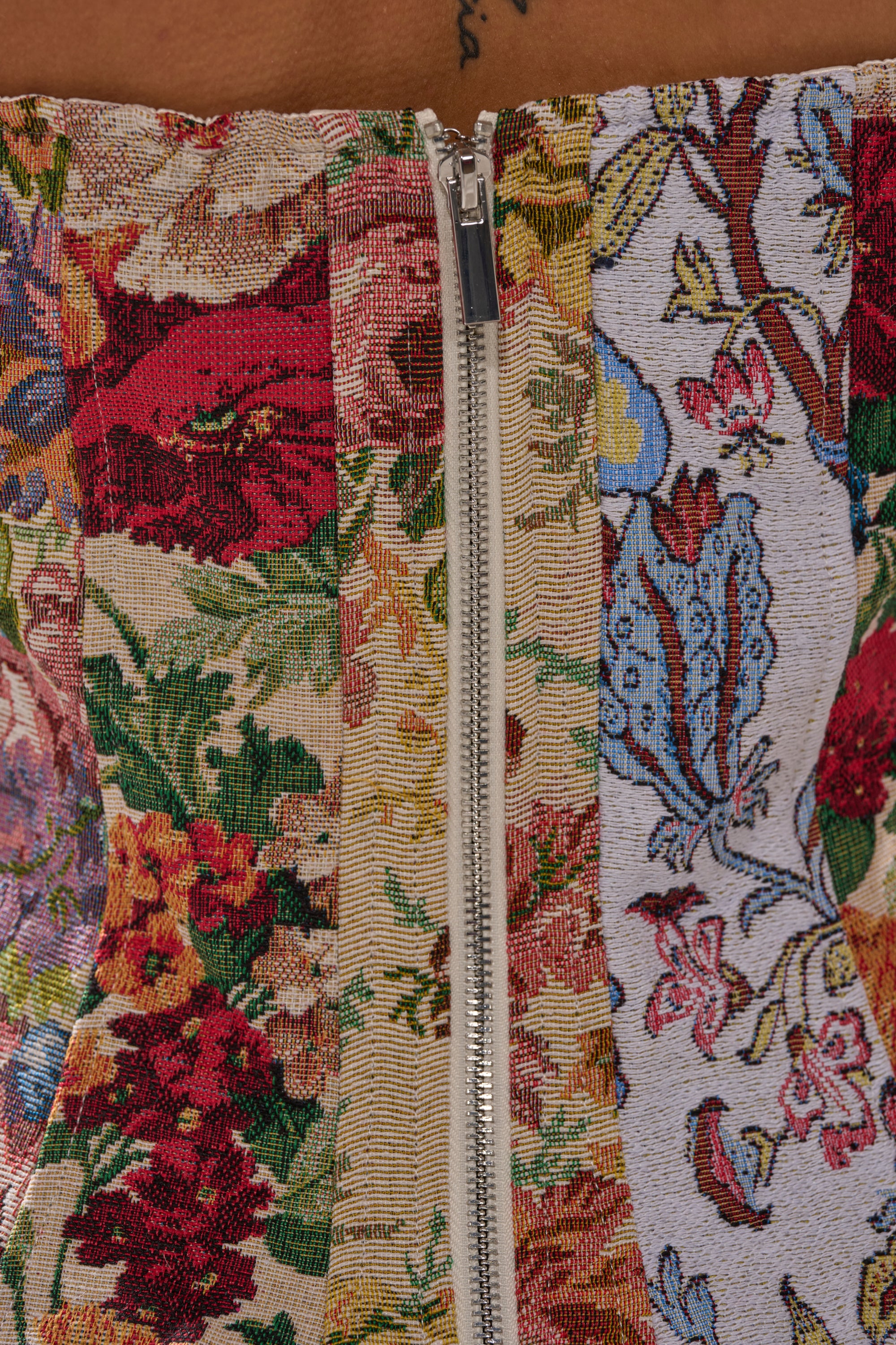 Close-up of the SUNDAY PATCHWORK CORSET, crafted from floral tapestry with red, yellow, and blue flowers on multi-patterned panels. Features a silver front zipper and green leaf accents for a vibrant look.