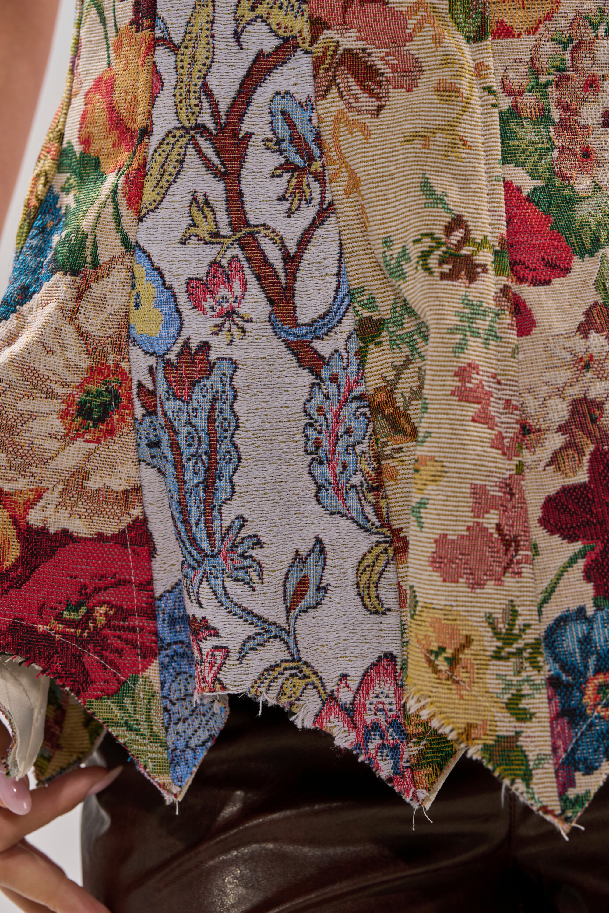 Close-up of the SUNDAY PATCHWORK CORSET, featuring a colorful, textured tapestry fabric with a red, yellow, blue, and green floral pattern, shown draped over dark brown leather pants.