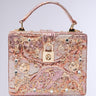 The BROCADE BABE TRUNK BAG is a luxurious rectangular bag with ornate pink and gold baroque brocade, metallic hardware, jewels, intricate pattern, top handle, gold clasp lock at the front, and a neutral light gray background.