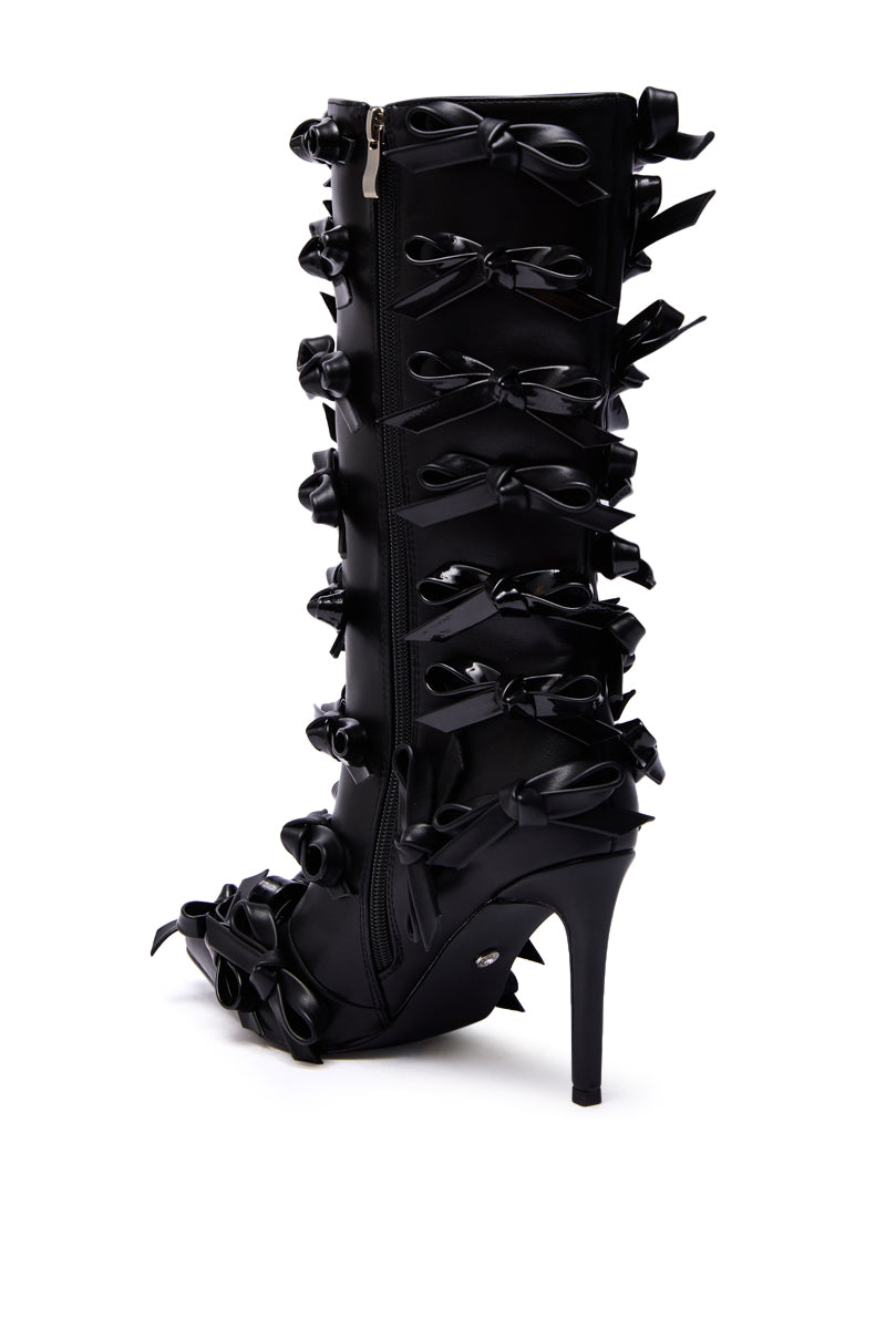 The AZALEA WANG TELMO BLACK BOW EMBELLISHED BOOTIE is a black knee-high stiletto bootie with a pointed toe, multiple black satin bows on the side, a sleek faux leather finish, and an easy side zipper.