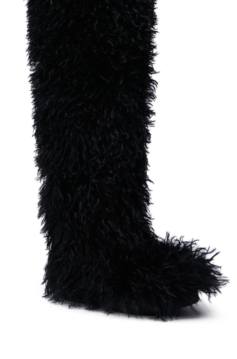 The image features a close-up of the AZALEA WANG TEMPLETON Black Poodle Fur Over the Knee Boot. This tall boot, with its shaggy black fur texture, covers the foot and extends up the leg. Just one stunning boot is visible against a plain white background.