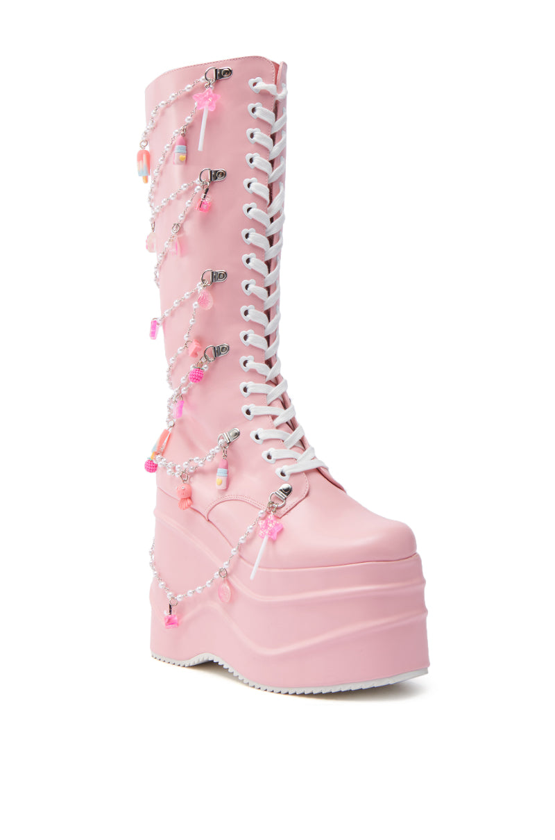 Step into kawaii style with KOI FOOTWEAR THE DREAMSCAPE NOVELTY PINK FLATFORM BOOT, crafted in shiny faux leather. Features white laces, chains, beads, and pink and white charms on a chunky platform sole.