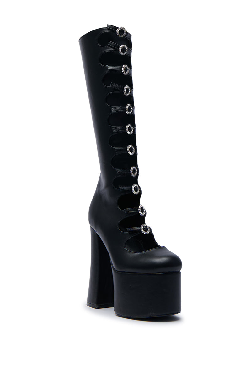 The AZALEA WANG TOMLIN BLACK BOOT is a sleek and stylish black mid-calf platform boot with a high heel, showcasing multiple circular cutouts up the leg. Each cutout is adorned with a silver ring detail, and the faux leather boot features a glossy finish.