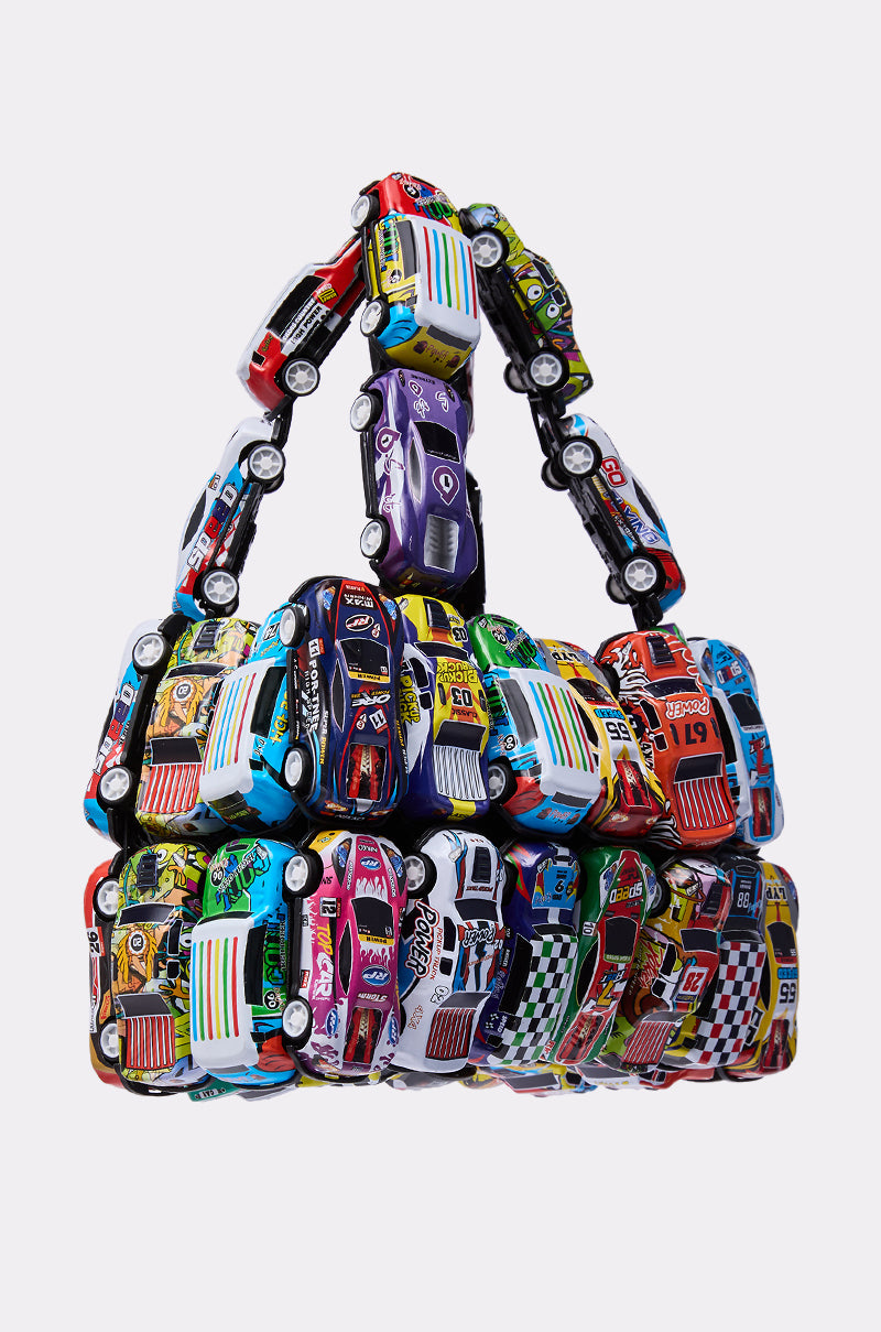 The I GO FAST RACE CAR PURSE is a playful handbag crafted from colorful toy race cars arranged in rows with a handle, shown against a plain white background.