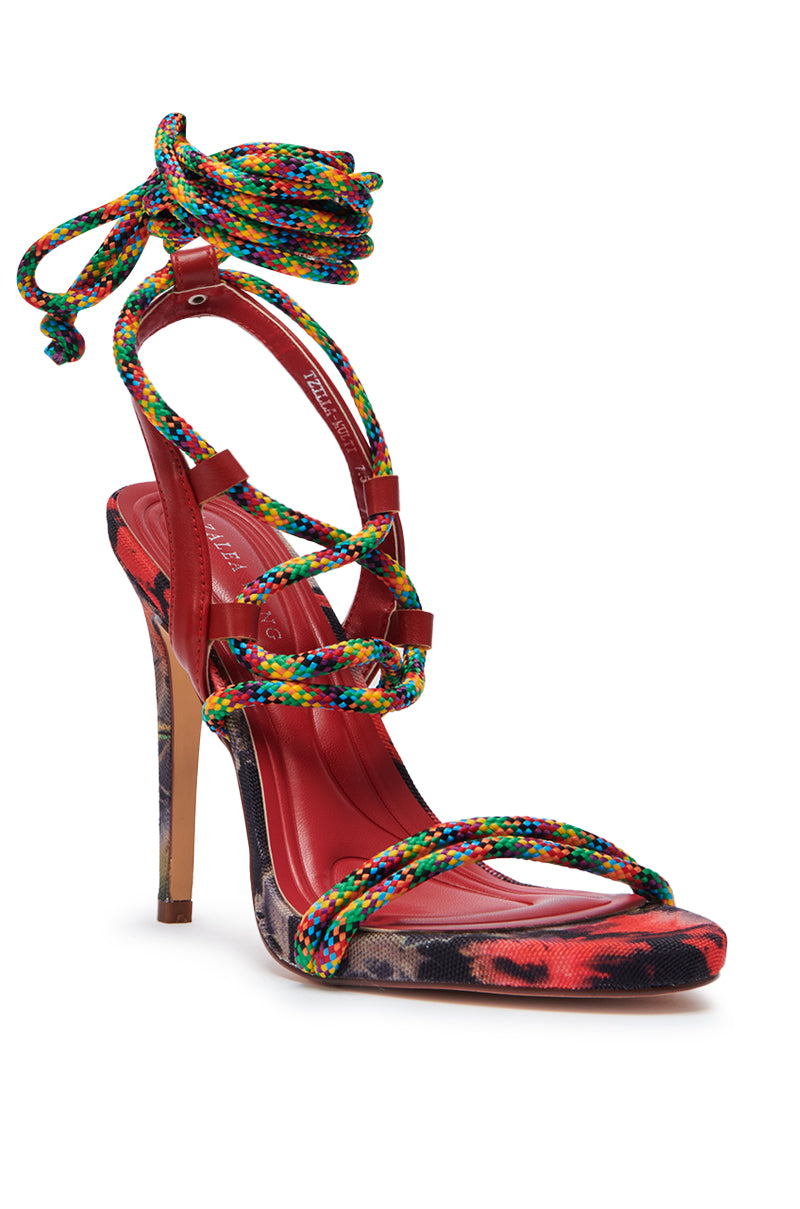 The AZALEA WANG TZILLA MULTI COLOR ROPE STILETTO SANDAL showcases a red base, floral print sole, and multicolor braided ankle straps that tie around the ankle. A tall stiletto heel completes this bold and elegant look.