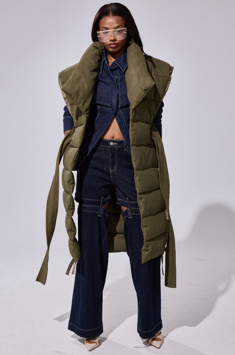 Wearing the PILOT JONES LONGLINE PUFFER VEST IN CROC SUEDE over a dark denim jacket and wide-leg jeans with strap details, this look is finished with pointed-toe heels and stylish sunglasses for a bold statement.