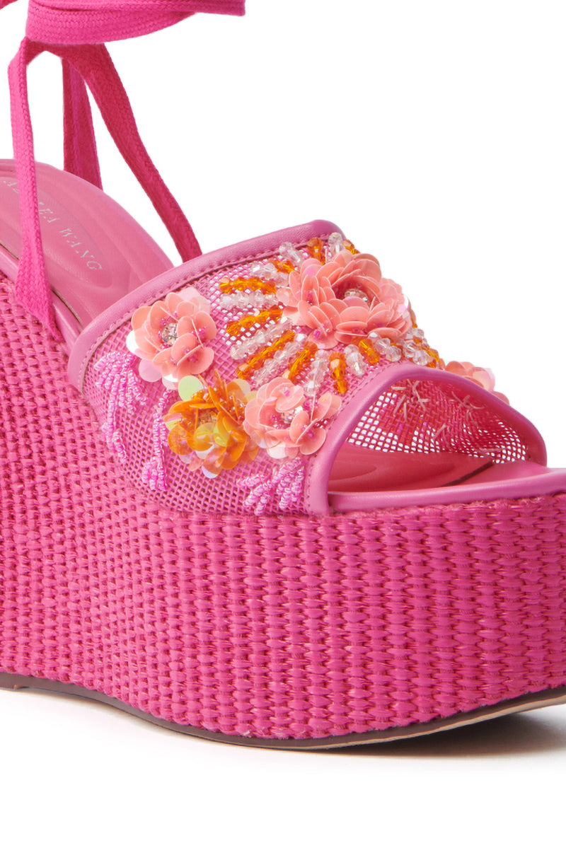 Close-up of the AZALEA WANG VONDA PINK WEDGE SANDAL, showcasing its vibrant pink color and tall woven platform sole. The sandal is adorned with intricate floral embellishments featuring pink and orange flowers and beads on the strap for a textured, decorative appearance.