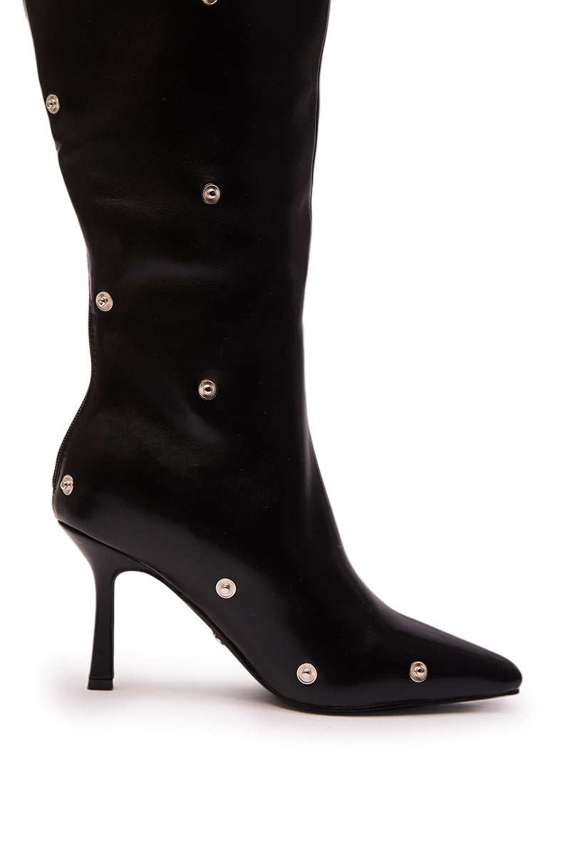 The AZALEA WANG VULTURE BLACK SHERPA LINED BOOT is a black, knee-high faux leather boot with a pointed toe, stiletto heel, silver snap button details on the side and back, and a cozy sherpa lining.