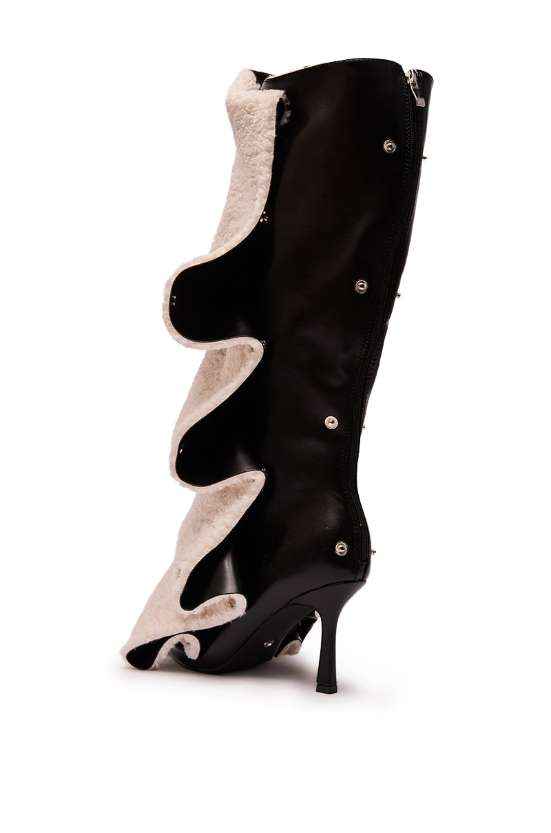 The AZALEA WANG VULTURE BLACK SHERPA LINED BOOT is a faux leather knee-high with black sherpa lining, wavy white shearling trim, and silver snap buttons along the side for an avant-garde, sculptural look.