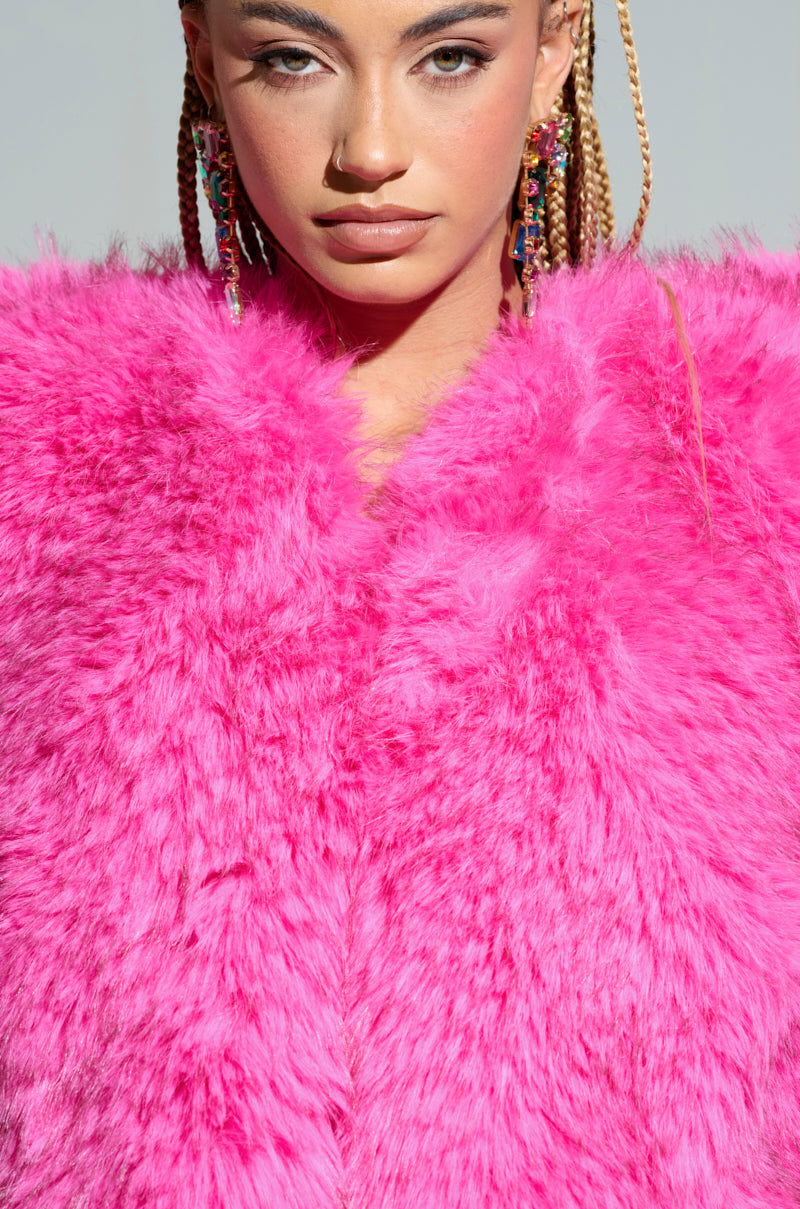A woman with braided hair and colorful earrings wears the vibrant STAR CROSSED LOVER FAUX FUR HEART VEST. The close-up portrait highlights her stylish attire against a plain background.
