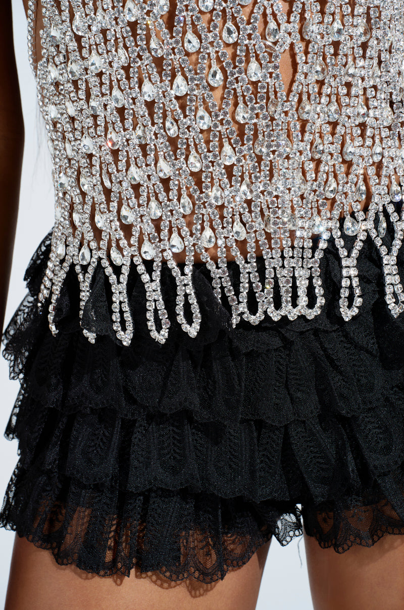 The LOREN Rhinestone Halter Neck Top in Silver features intricate chain detailing above a layered black lace skirt, blending elegance with edginess. The delicate silver chains create a striking contrast against the textured ruffles of the skirt.