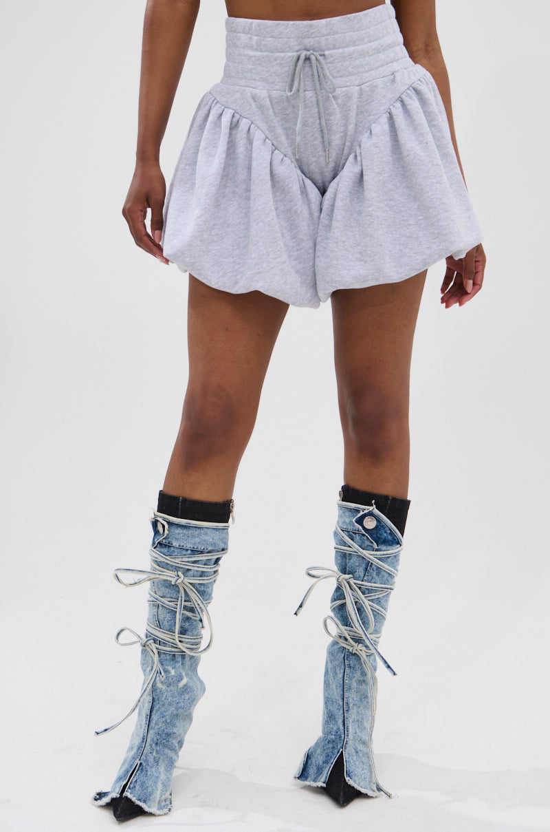 A person wears HEATHERED BUBBLE SHORT in light gray cotton with a high-rise fit, paired with knee-high light blue lace-up denim boots, standing against a plain white background.