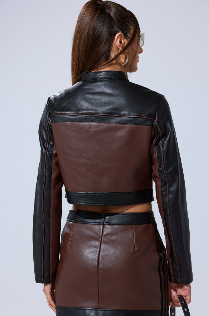 A woman with long brown hair, wearing sunglasses and the NO PICTURES PLEASE CROPPED MOTO jacket with a matching high-waisted skirt, is shown from the back against a plain light background.