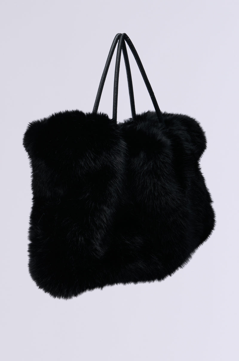 The YETI LARGE FAUX FUR TOTE IN BLACK, featuring a soft, fluffy texture and two thin handles, stands against a plain background. Its luxurious appearance makes it a perfect addition to winterize your wardrobe.