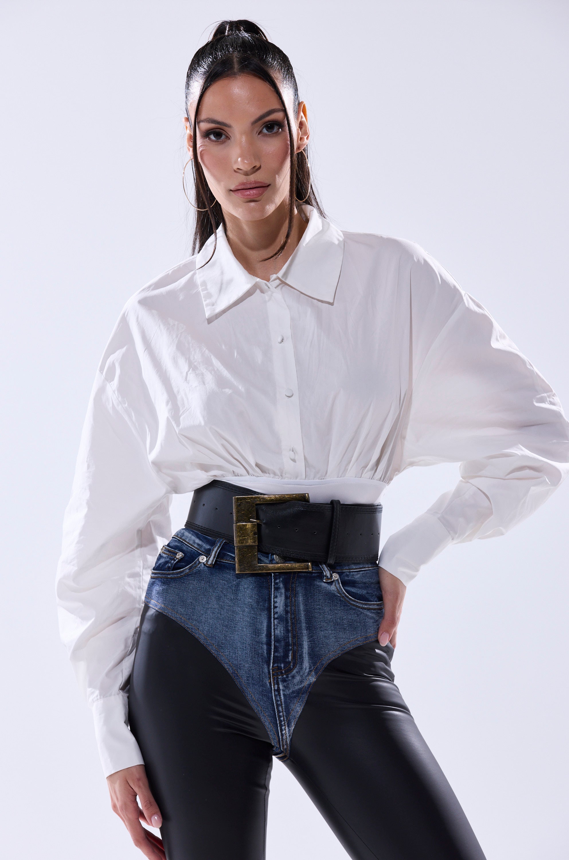 A woman wears the LET'S GO BABY BODYSUIT, black high-waisted leggings, and unique jean shorts with a large faux leather belt, standing against a plain light background.