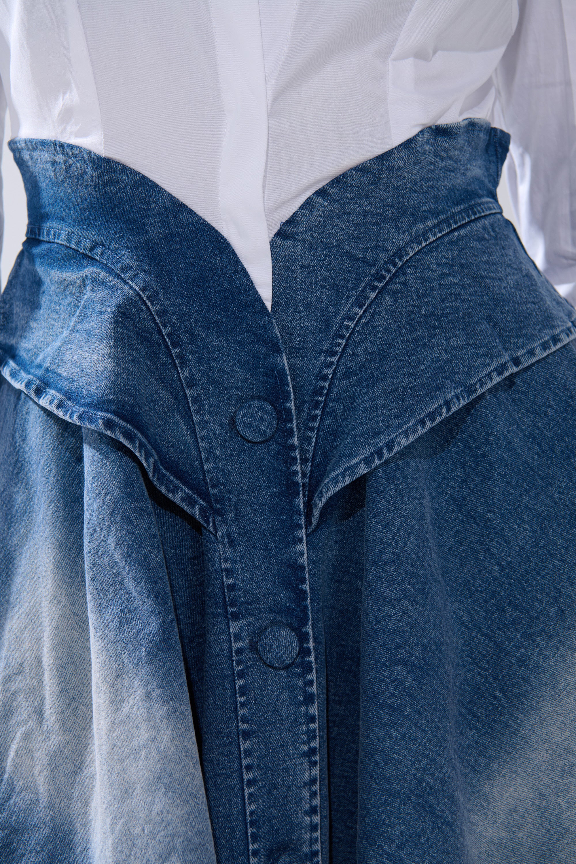 A close-up of a person wearing the DONT NEED NOBODY DENIM MINI DRESS features a white shirt tucked into its high-waisted, buttoned, and folded-waist design for a chic look with faded, textured blue denim.