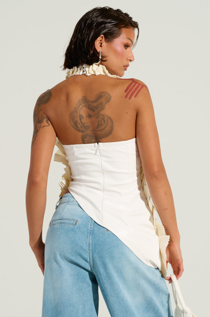 A person with tattoos on their back is wearing the "COVER ME IN LOVE TOP," a white piece featuring an asymmetrical hem, paired with blue jeans. Their short, dark hair is styled away from the face. The image captures a side and back view, highlighting both the unique clothing style and the intricate tattoos.