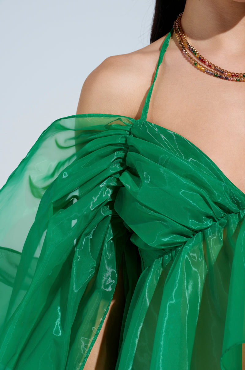 A close-up shows a person wearing AN ELEGANT EVENING ORGANZA BLOUSE in vibrant Kelly Green with gathered fabric and a halter strap, styled with layered, colorful bead necklaces. The sheer, off-shoulder design highlights the upper body and part of one arm.