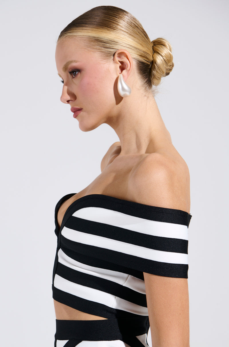A person with blonde hair in a bun is wearing the WAITING FOR YOU STRIPE BLOUSE, which has classic black and white stripes. They have a large white earring and are gazing thoughtfully to the side against a plain background.