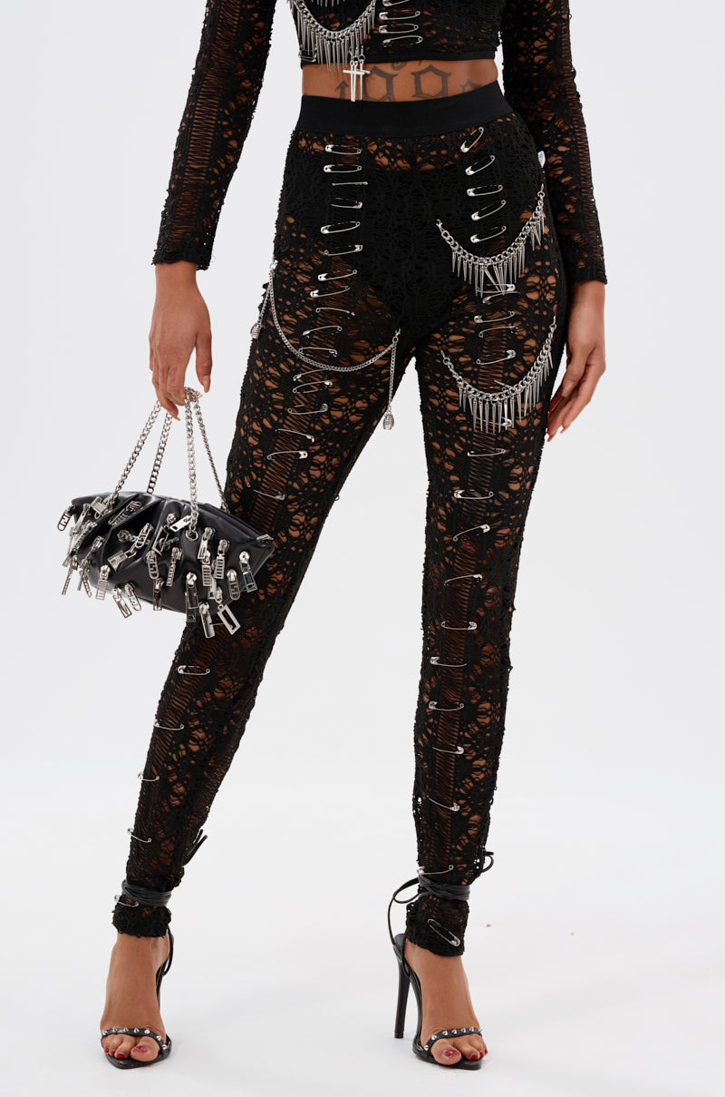 A person wearing the TRY ME LACE LEGGING with edgy details, accessorized with a black chain-trimmed handbag and black high-heeled sandals. Only their body is visible; their face is not shown.