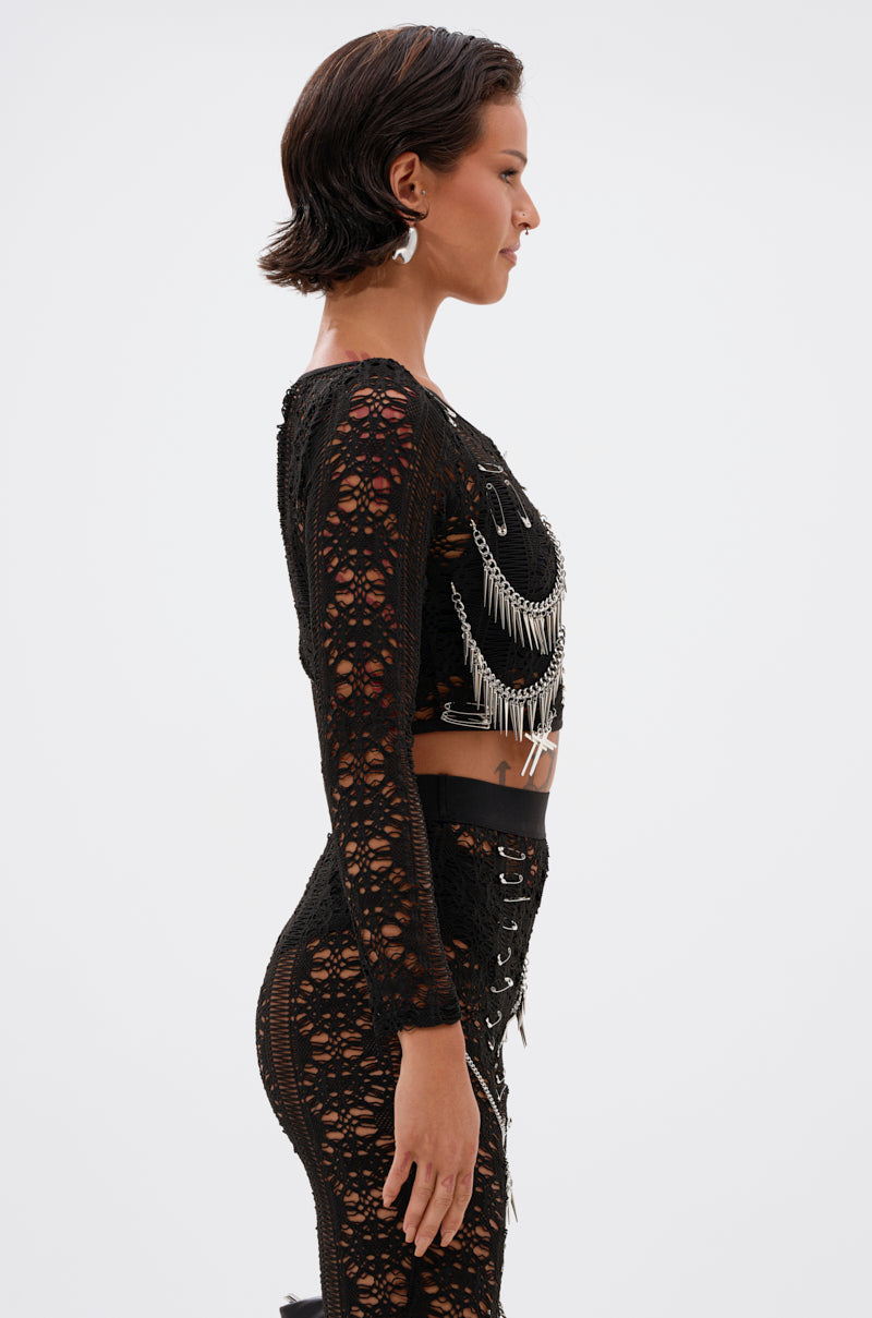 A woman with short dark hair stands in profile, wearing the TRY ME LACE LONG SLEEVE WITH PINS. The plain light background highlights her fitted, edgy style.