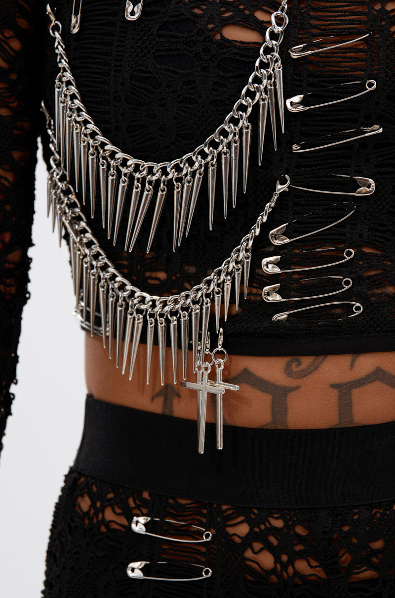 A close-up shows someone wearing the TRY ME LACE LONG SLEEVE WITH PINS—an edgy, cropped lace top adorned with silver safety pins, spiked chains, and a cross pendant. A tattoo is visible beneath the sheer fabric.