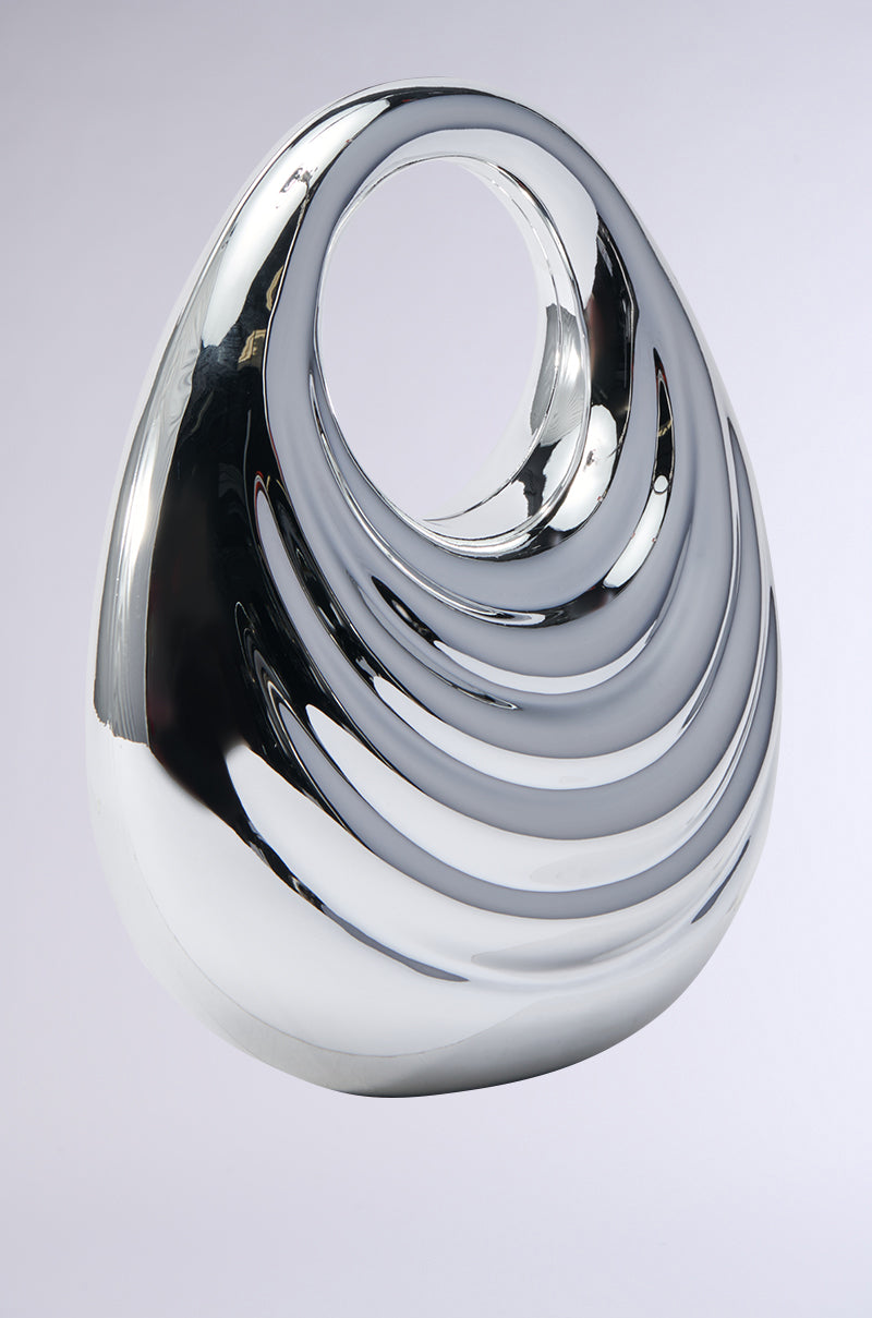 The STAY IN MY LANE ACRYLIC PURSE boasts a sleek, modern design with its smooth, flowing curves and prominent circular opening near the top. Set against a neutral background, its reflective metallic-like surface creates dynamic, swirling reflections akin to an avant-garde accessory in motion.