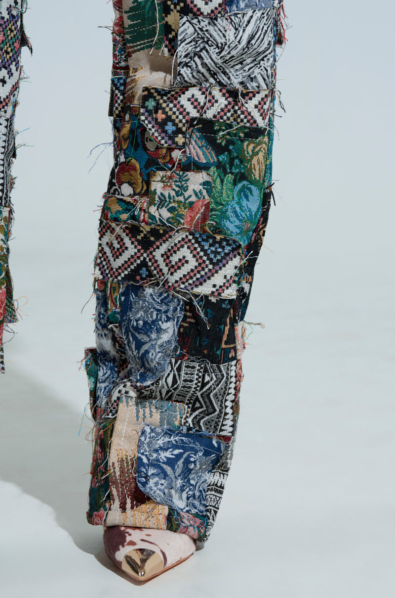 Close-up of ODESSA RELAXED FIT PATCHWORK PANTS with vibrant floral and geometric patterns in quilt-like tapestry, revealing a pointed shoe underneath.