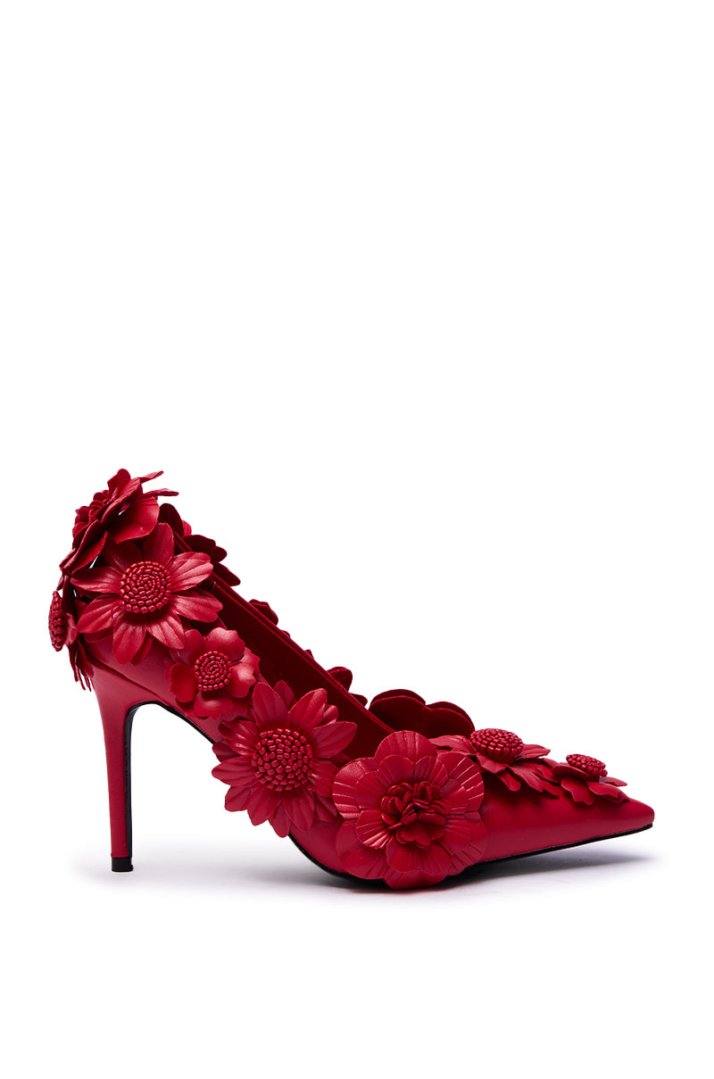 The AZALEA WANG ZARAH RED FLOWER PUMP is a high-heeled, pointed-toe faux leather stiletto in red, featuring 3D red flowers and petals along the side and heel, displayed on a plain white background.