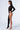 A person is wearing the ICONS ONLY STRETCH BODYSTOCKING, a distinctive black bodysuit featuring geometric cutouts that envelop the entire left side of their body, including one arm and one leg, while leaving the right arm and leg exposed for an asymmetrical silhouette. They are standing in profile view against a plain white background, accessorized with clear high-heeled shoes.