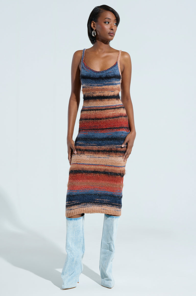 Confidently, a person showcases the curve-hugging silhouette of the UP ALL NIGHT MIDI DRESS, featuring multicolor stripes in shades of blue, orange, and brown. They complement it flawlessly with light blue knee-high boots against a simple, minimalistic backdrop.