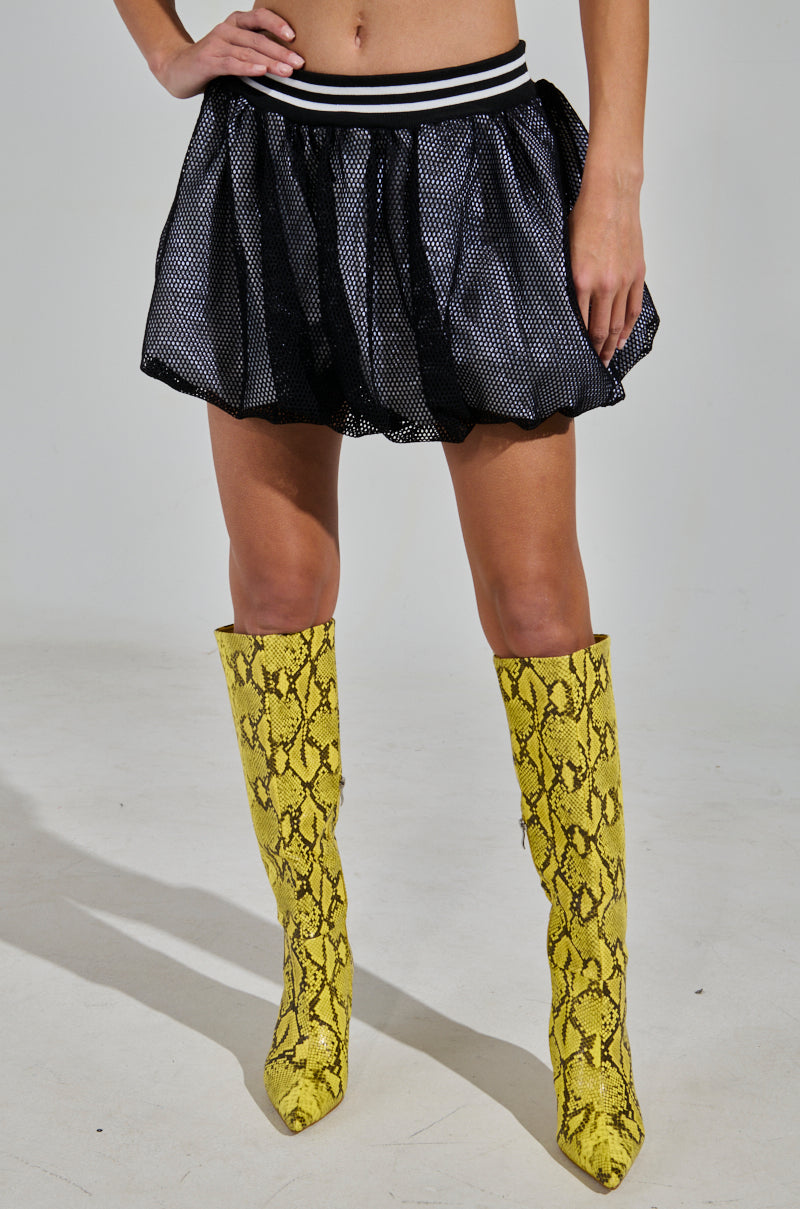 A person wearing the PLAYERS ONLY JERSEY BUBBLE SKIRT, featuring a black mesh design with striped waistband, paired with yellow snakeskin-patterned knee-high boots exudes a sporty-chic vibe against a simple backdrop. The focus is on their torso to feet, emphasizing their bold fashion statement.