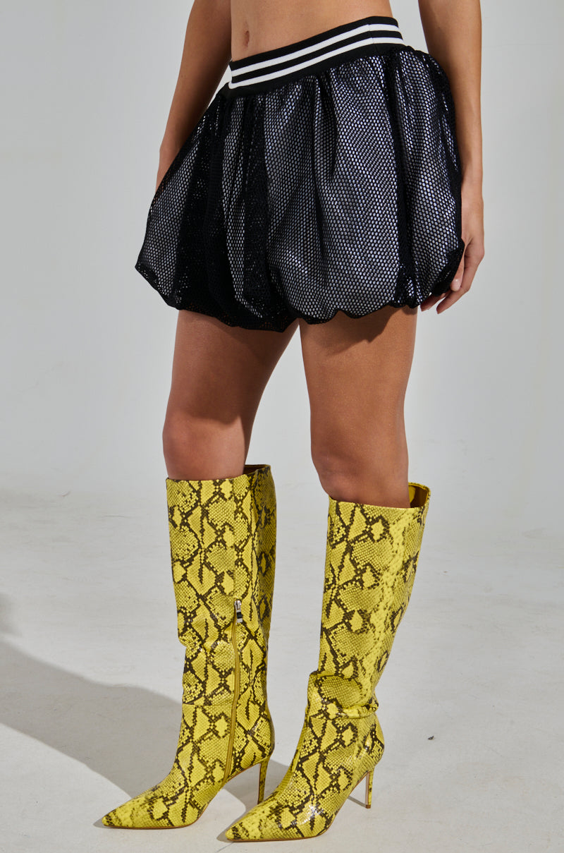 Sporting a chic look, a person stands confidently against a plain light background in knee-high yellow snake print boots and the PLAYERS ONLY JERSEY BUBBLE SKIRT, featuring a black shimmer finish with a white-striped waistband.
